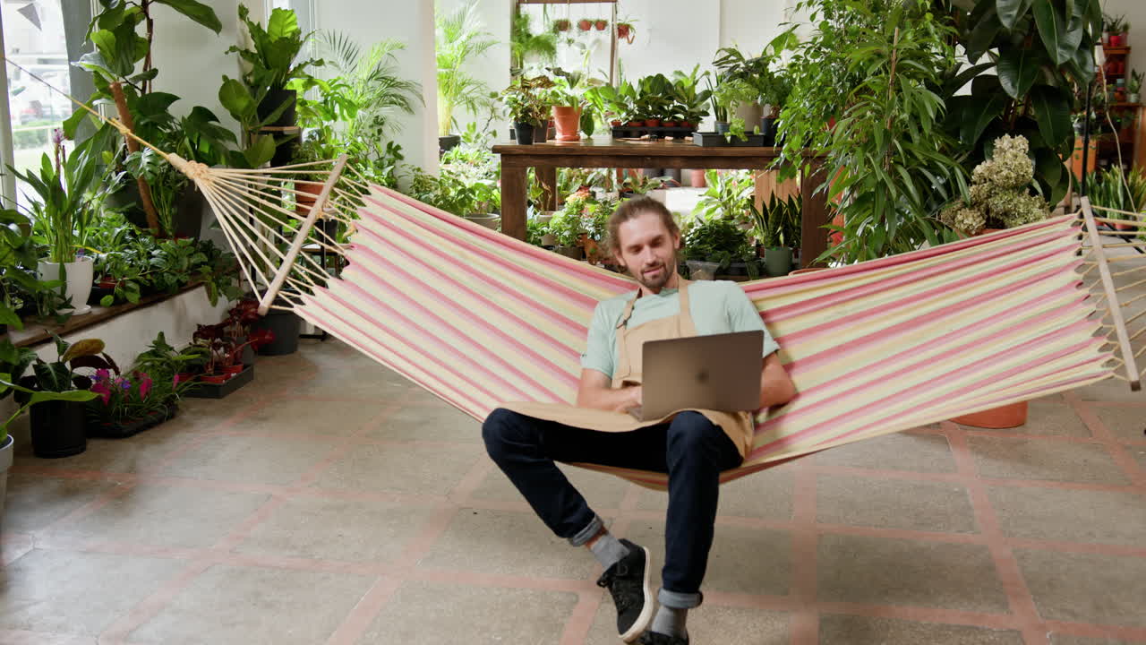 hombre trabajando en una computadora portátil en una hamaca en una tienda de flores