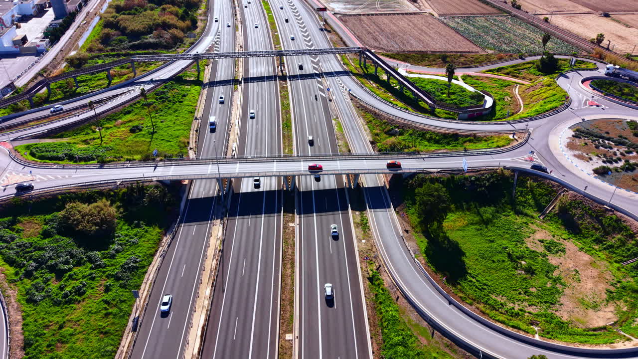 Complejo sistema de autopistas con coches, carreteras asfaltadas, césped verde y puentes en España. Vista aérea de un cruce de autopistas de varios niveles