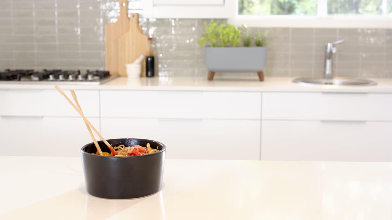 Black bowl of noodles with chopsticks on modern kitchen countertop, copy space