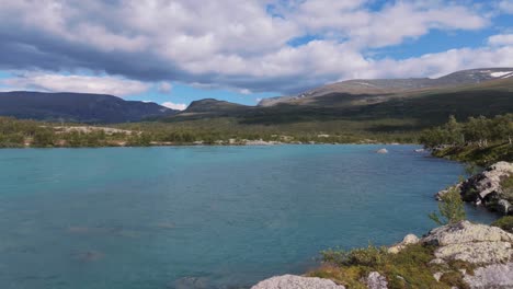 vista aérea de un lago prístino rodeado de costas rocosas y vegetación exuberante en besseggen, innlandet, noruega, con montañas en el fondo