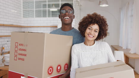 portrait of smiling young couple carrying boxes into new home on moving day