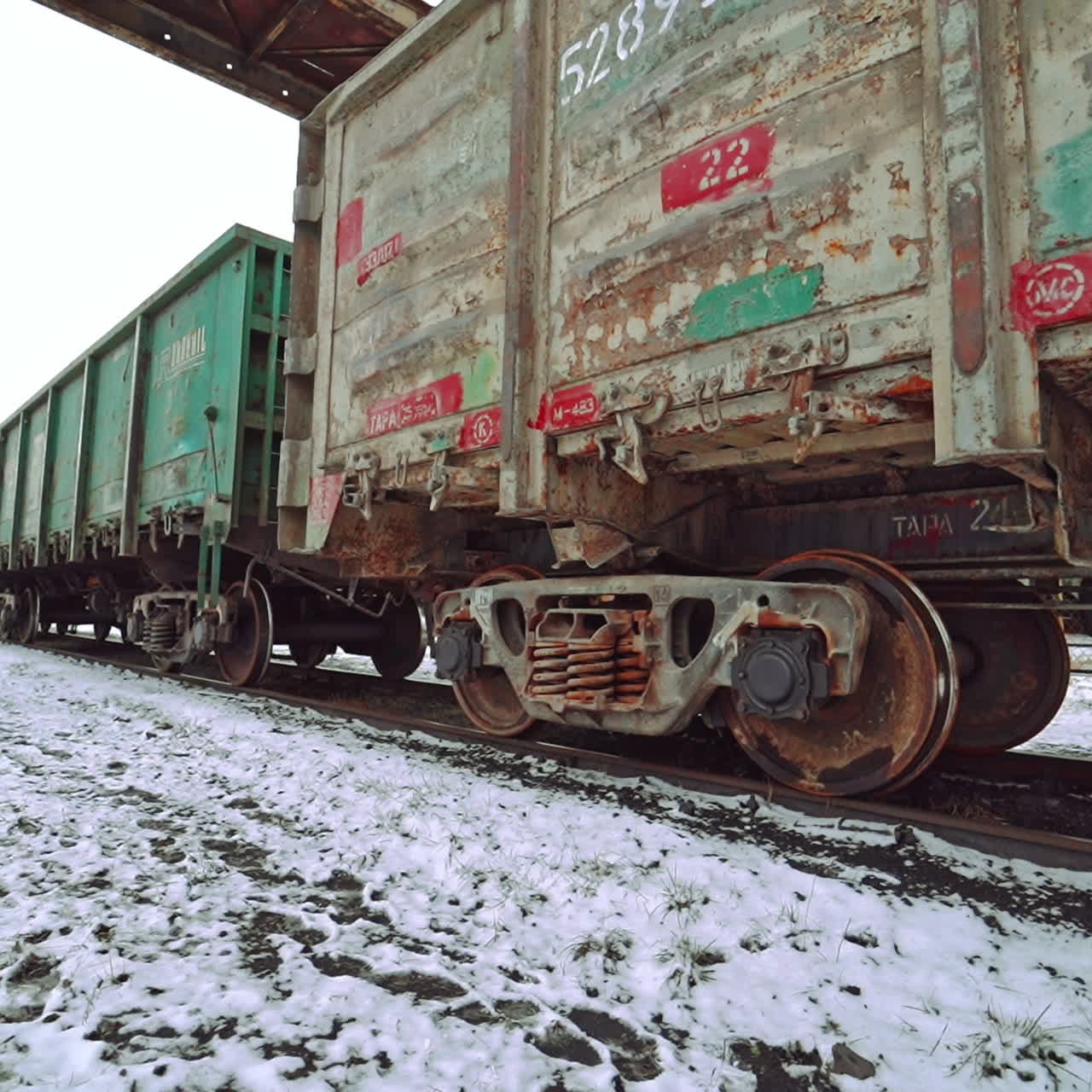 Row of multi-colored containers for cargo rides along the rails at the railway station and stops on the background of the ground covered with snow. View of bottom. Close-up.