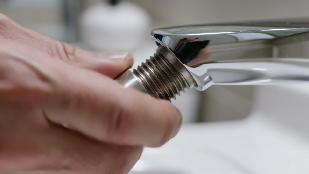 Gripping adult male hands rotating threaded aerator on chrome faucet, removing insert to inspect