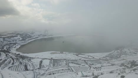 Drone-aerial-view-of-Lake-Ram-and-village-under-heavy-cloud-cover-and-snow,-Israel