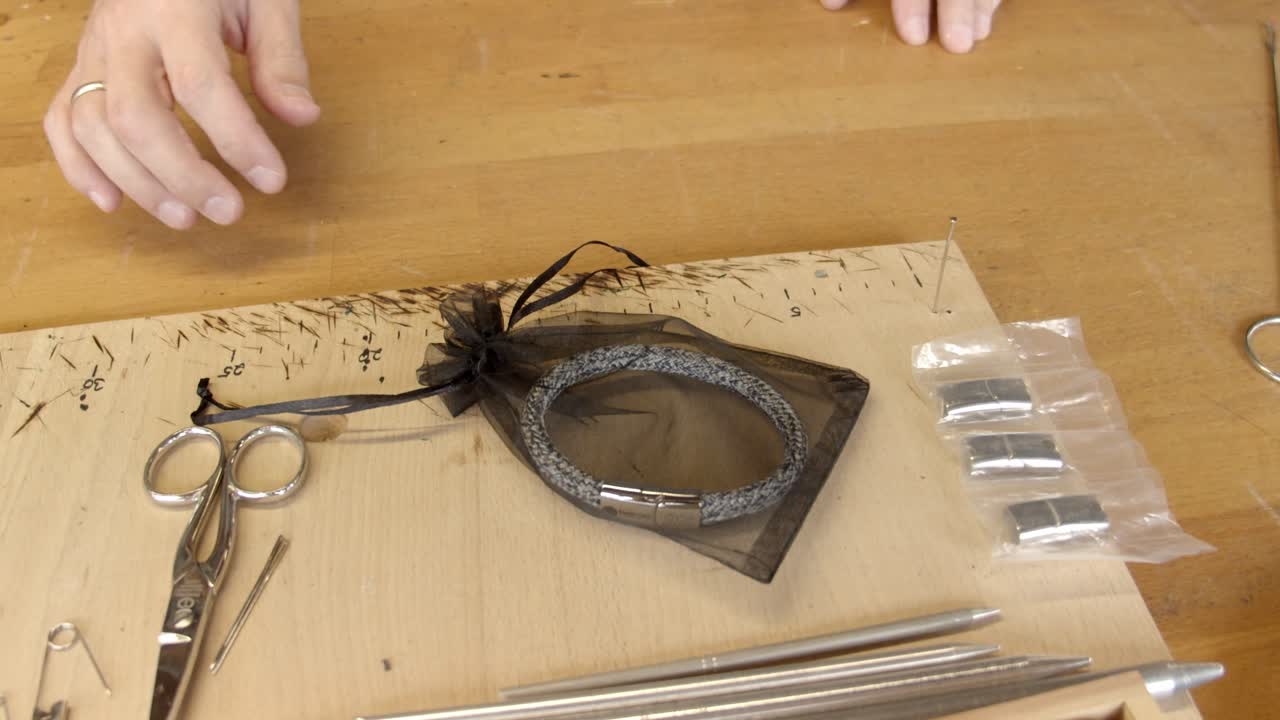 artesano poniendo una nueva pulsera de color plata envuelta para regalo en la mesa de elaboración del taller, vista en movimiento