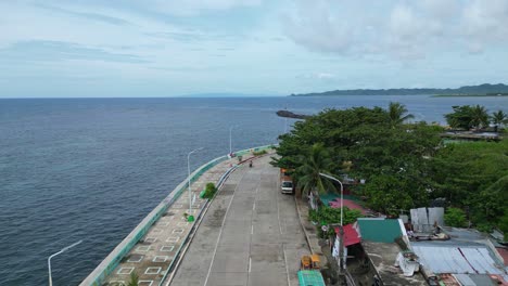 aerial overhead drone shot of road on seawall between beautiful ocean and small barangay in catanduanes, philippines