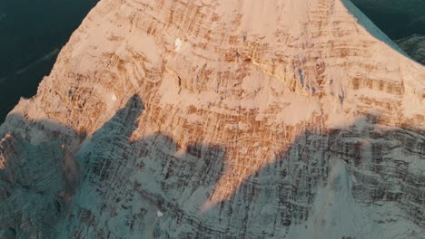 Drone-view-tilting-up-the-rugged-Tofana-di-Rozes-summit-in-the-Dolomites-revealing-the-massive-Monte-Pelmo-peak-in-the-background-at-sunrise