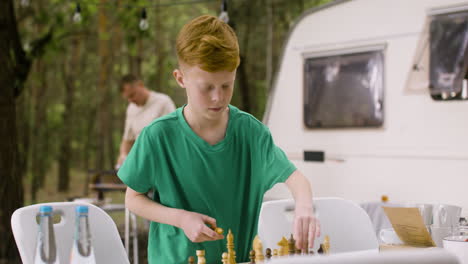 Kleiner-Junge,-Der-Auf-Dem-Campingplatz-Im-Wald-Ein-Schachbrett-Aufstellt