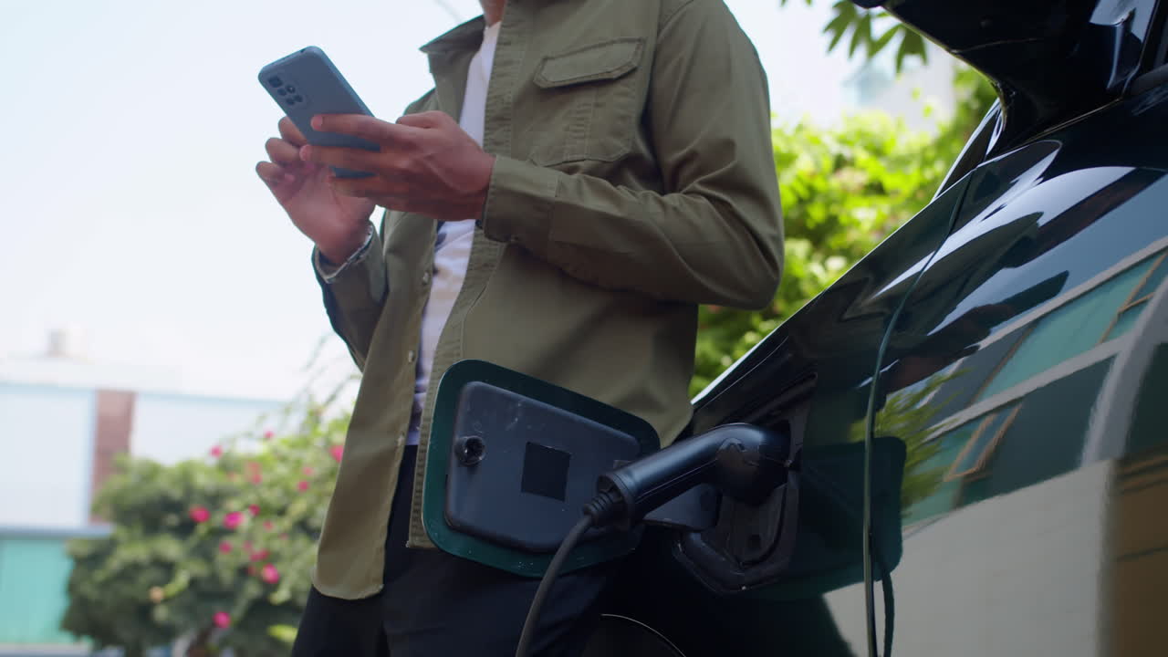 Man using smartphone while charging electric vehicle