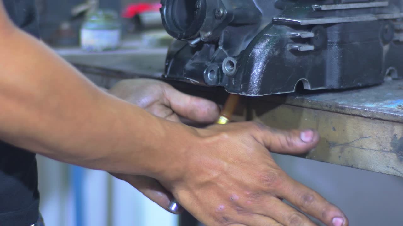 A mechanic is focused on repairing and adjusting various car engine components in a busy workshop.
