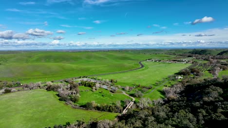 aerial view over oak trees on hill overlooking green rolling hills and blue sky, round valley regional preserve, california