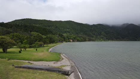 Aerial-view-of-the-Chapel-of-Nossa-Senhora-das-VitÃ³rias,-a-small-funerary-chapel-on-the-southwestern-corner-of-Lagoa-das-Furnas-in-the-civil-parish-of-Furnas-on-the-Azorean-island-of-SÃ£o-Miguel