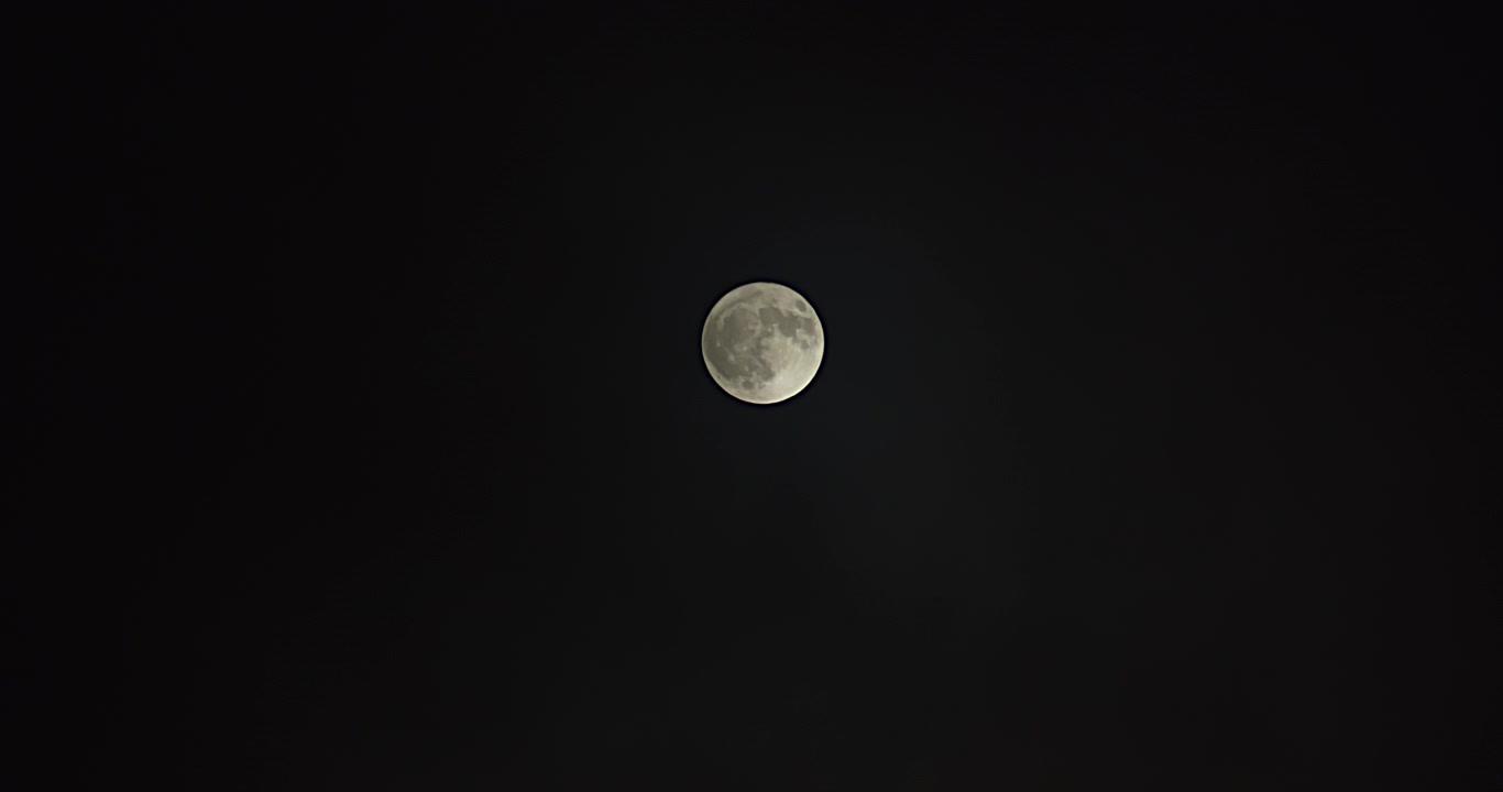 Plano aberto de uma lua cheia enquanto a névoa passa, revelando a lua cheia no final