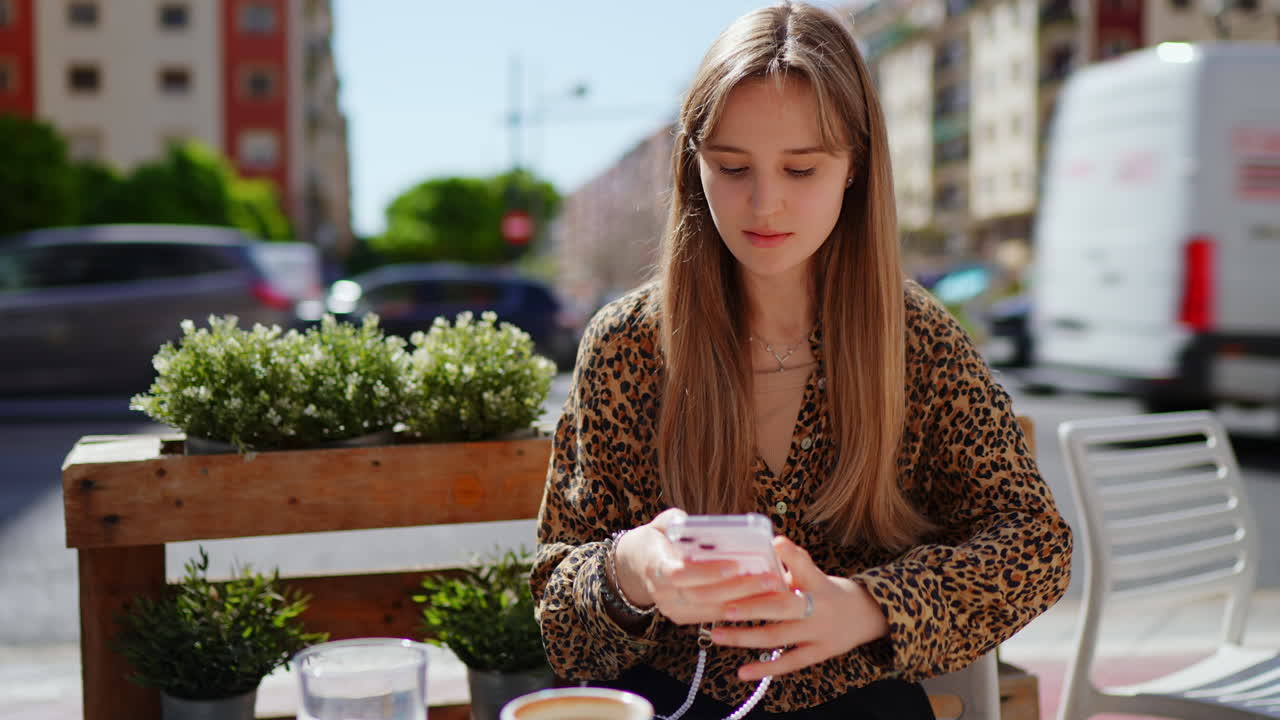 Young woman enjoying a coffee and using her mobile phone at an outdoor cafe