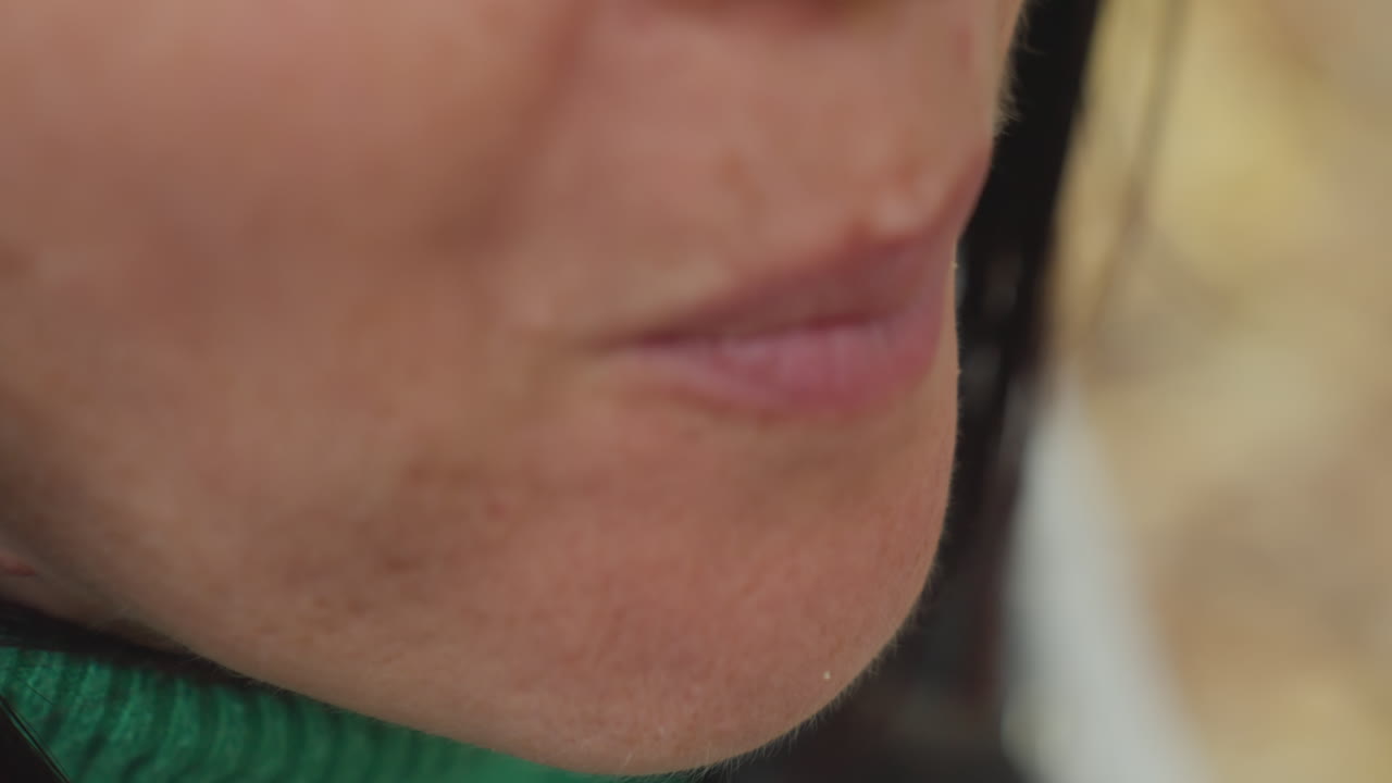 primo piano delle labbra di una donna all'aperto, labbra screpolate e secche su un maglione verde, sorriso accennato e bocca stretta, texture della pelle e rughe sottili visibili, vapore del respiro nell'aria invernale, stato d'animo intimo e contemplativo, cura della pelle