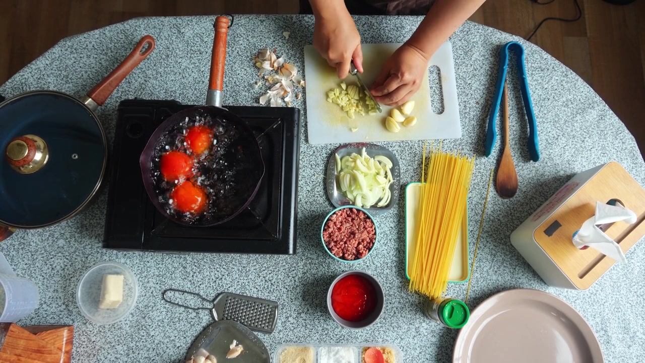 Vista dall'alto di un cuoco che trita finemente spicchi d'aglio, circondato da ingredienti colorati per la pasta