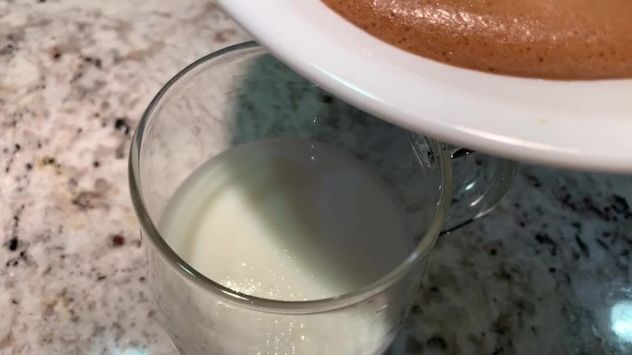 Dalgona Coffee drink. Slowly pouring over a thick frothy layer of whipped coffee over a glass of milk. This easy to make drink has gone viral over social media platforms.