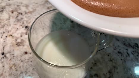 dalgona coffee drink. slowly pouring over a thick frothy layer of whipped coffee over a glass of milk. this easy to make drink has gone viral over social media platforms.