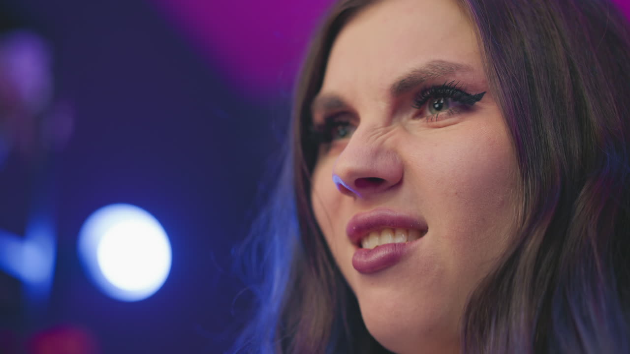 Close up of woman with expressive face chewing food while staring with stern look under intense studio lights, dramatic mood highlighted by vibrant lighting and deep shadows in background