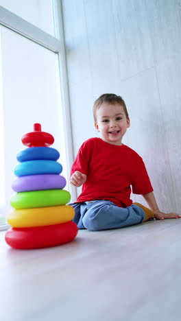 adorable happy baby boy plays with pyramid sitting on the floor. low angle view at the toddler kid playing joyfully at home. vertical video.