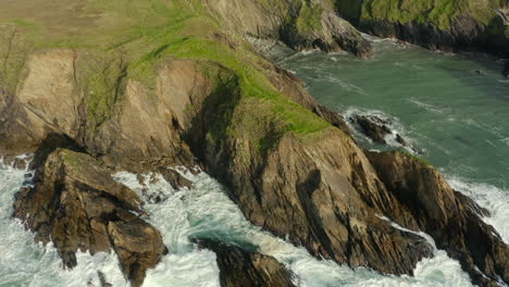 aerial view, tilt up shot in 4k, waves crash against the rocks, camera tilts up to reveal the beautiful green of ireland