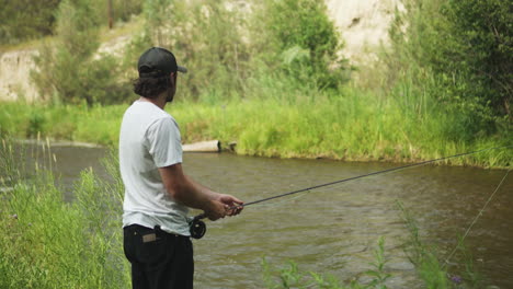 caucasian man fly fishing in fast-flowing river, lush green river bank