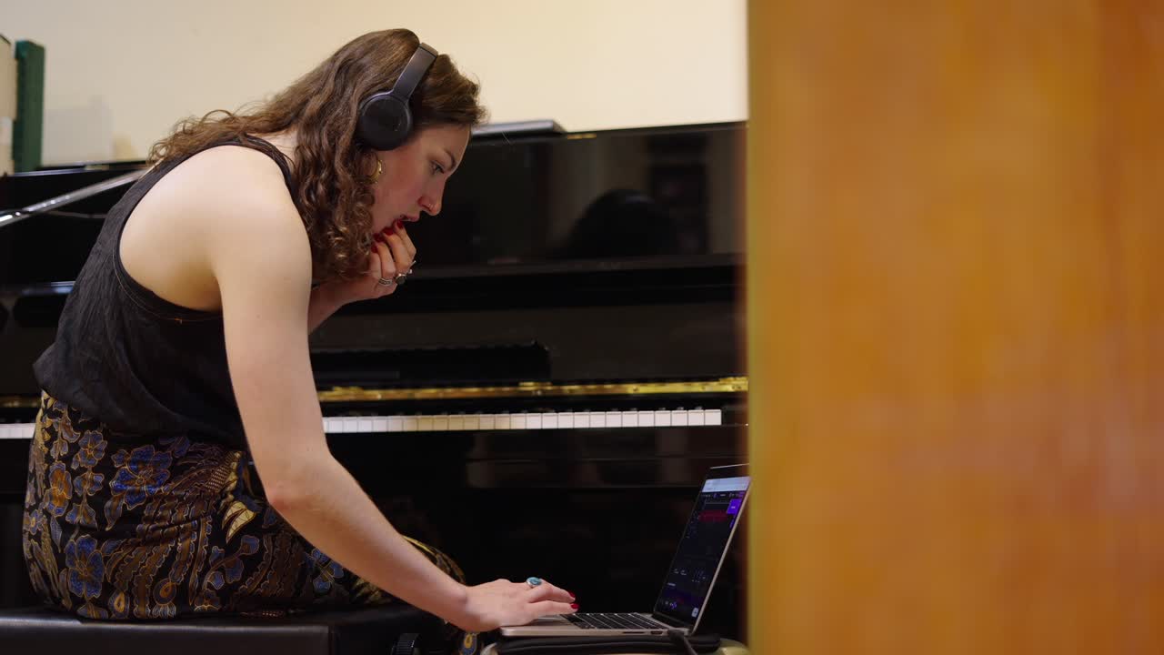 Young woman with headphones working on laptop at a piano