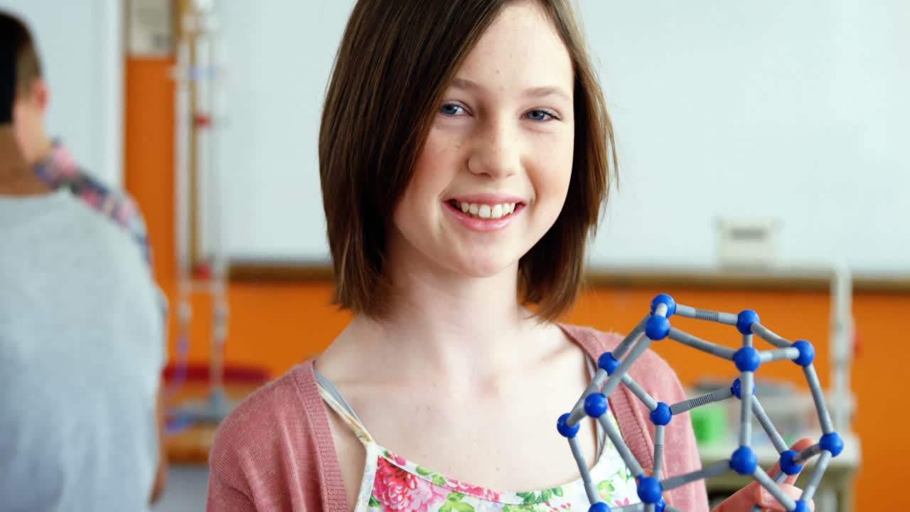 Portrait of happy schoolgirl experimenting molecule model in laboratory