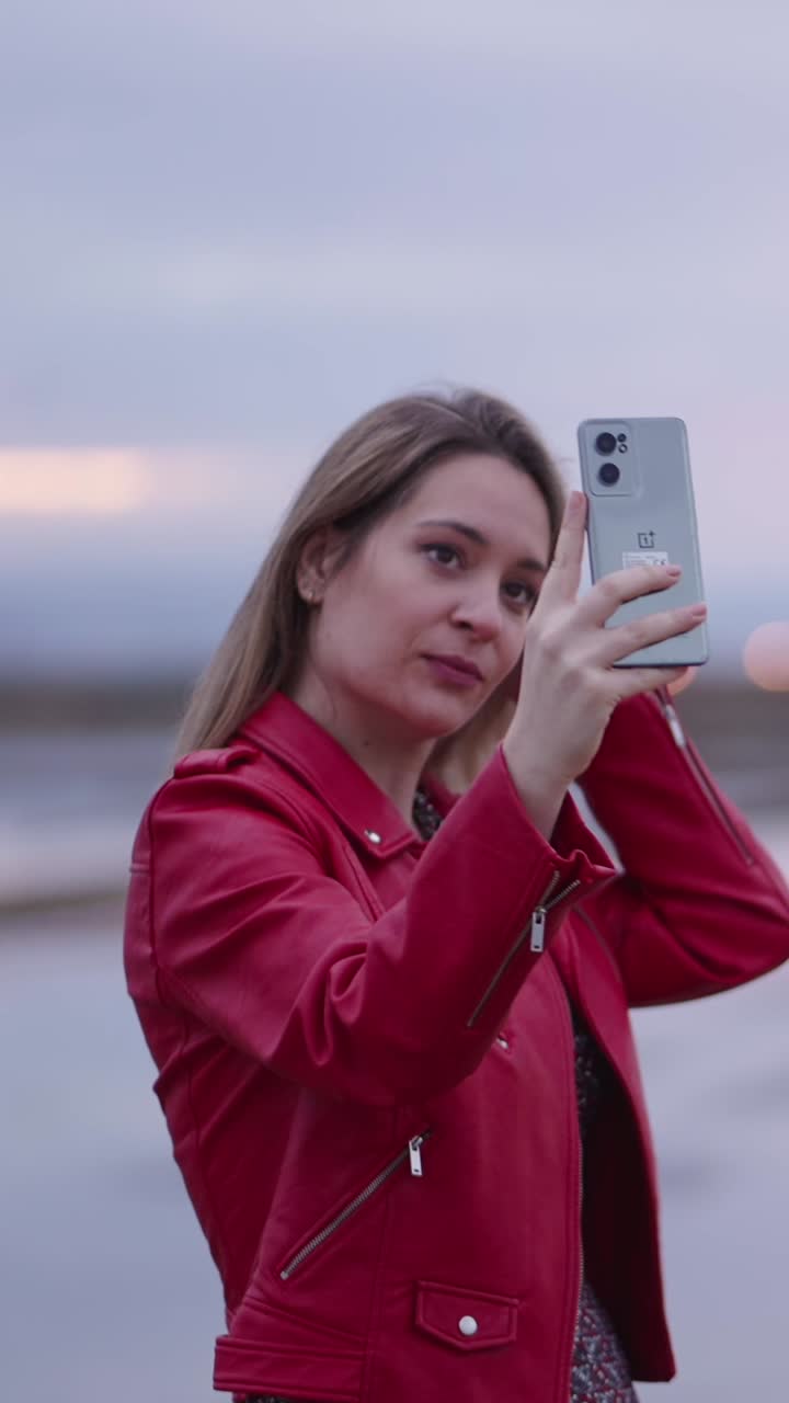 Mulher com jaqueta de couro vermelha tirando uma selfie ao pôr do sol