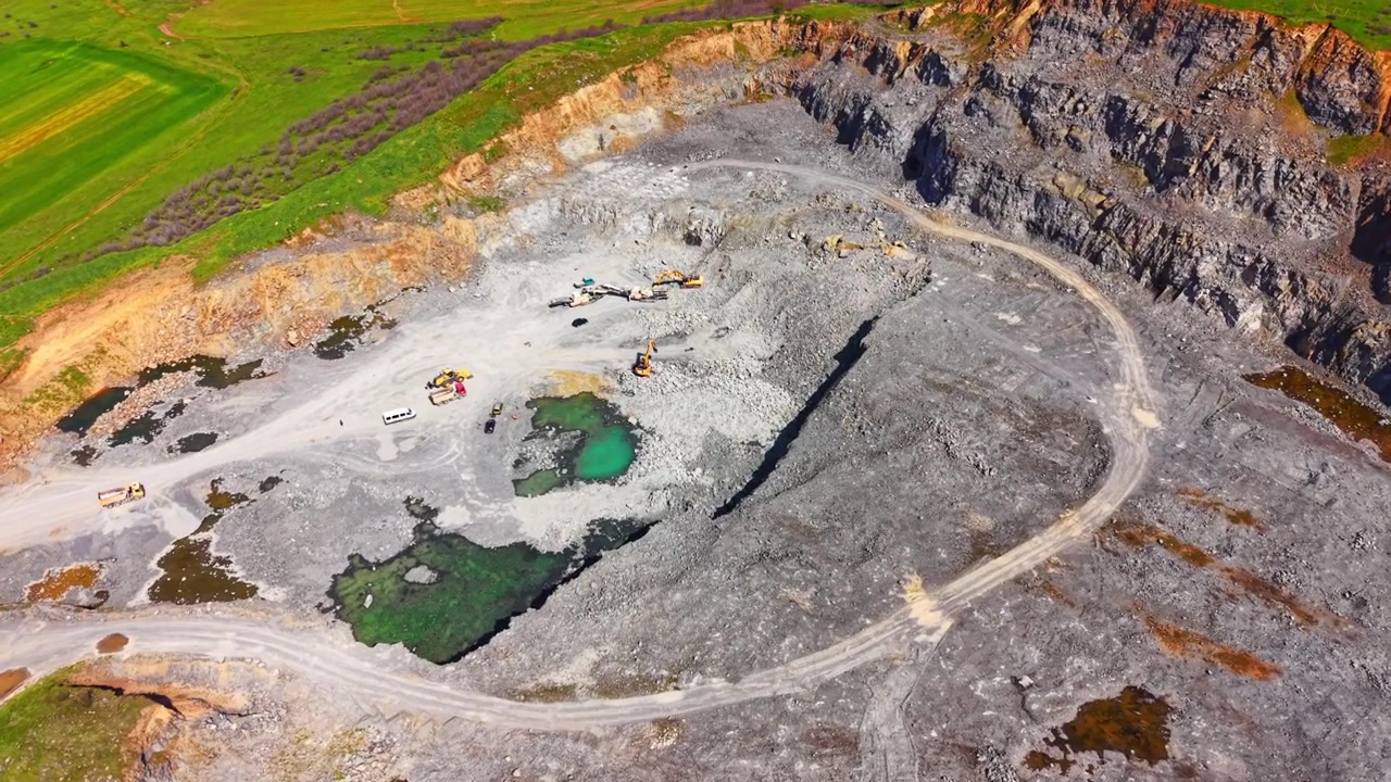 Elevated view of deep stone excavation site with machinery, trucks and emerald green water pools. Open pit industrial rock quarry, Burgas region, Bulgaria
