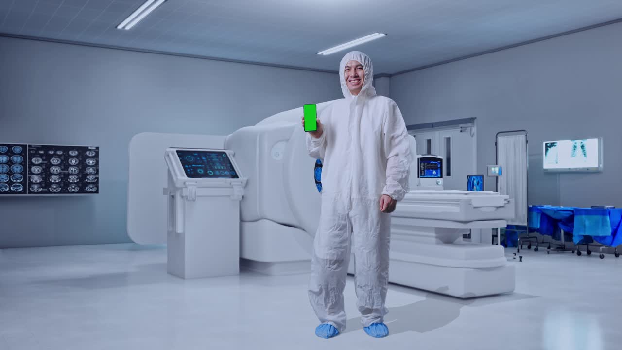 Full Body Of Asian Male Scientist Smiling And Showing Green Screen Smartphone While Standing With MRI Machine In The Hospital