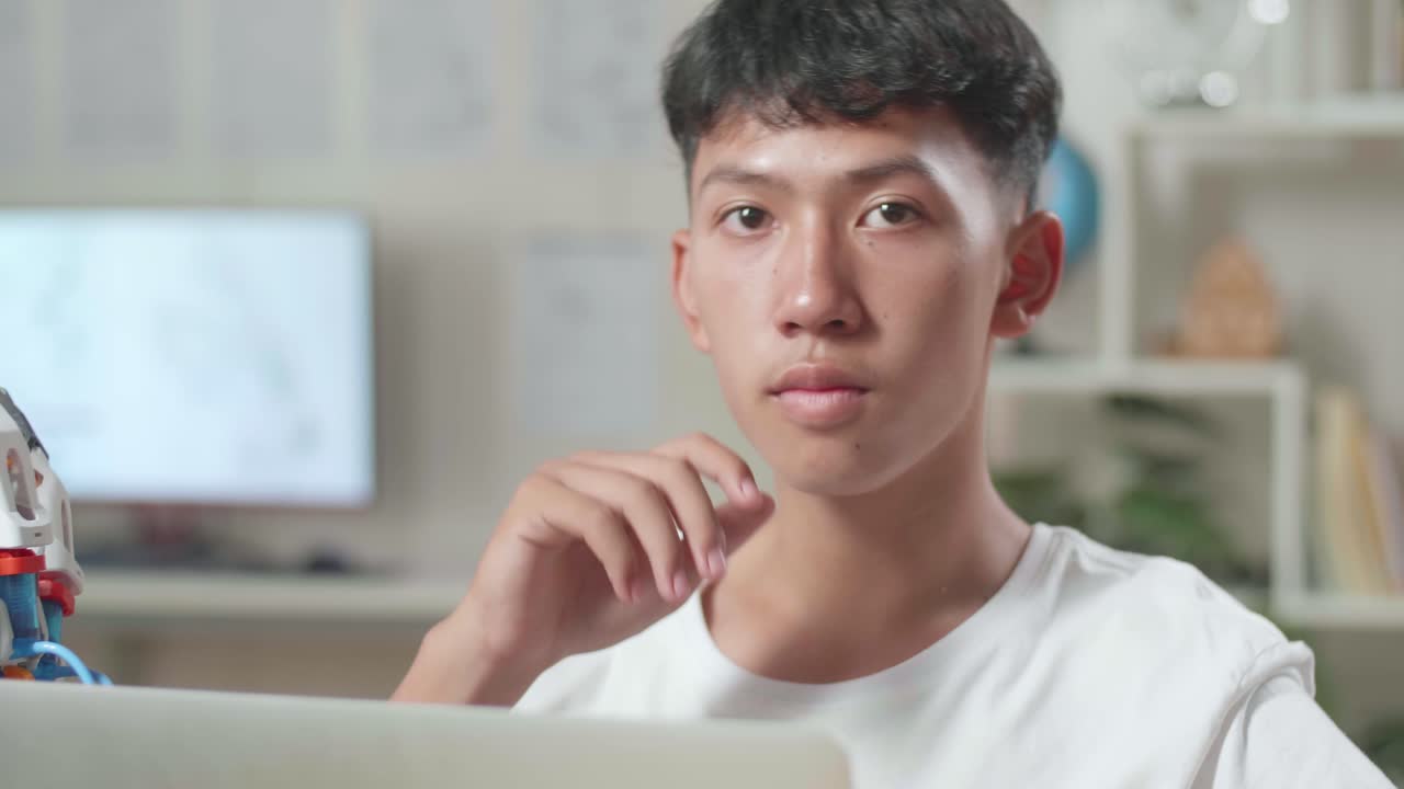 집에서 노트북에서 사이보그 손에 대해 작업하는 동안 생각하고 지표손가락을 올리는 아시아 소년의 클로즈업