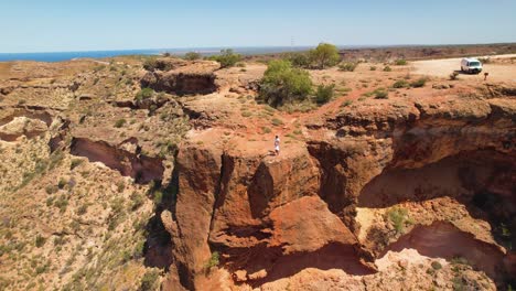 panoramic view of a vast red rock canyon with people on the cliff edge overlooking the ocean