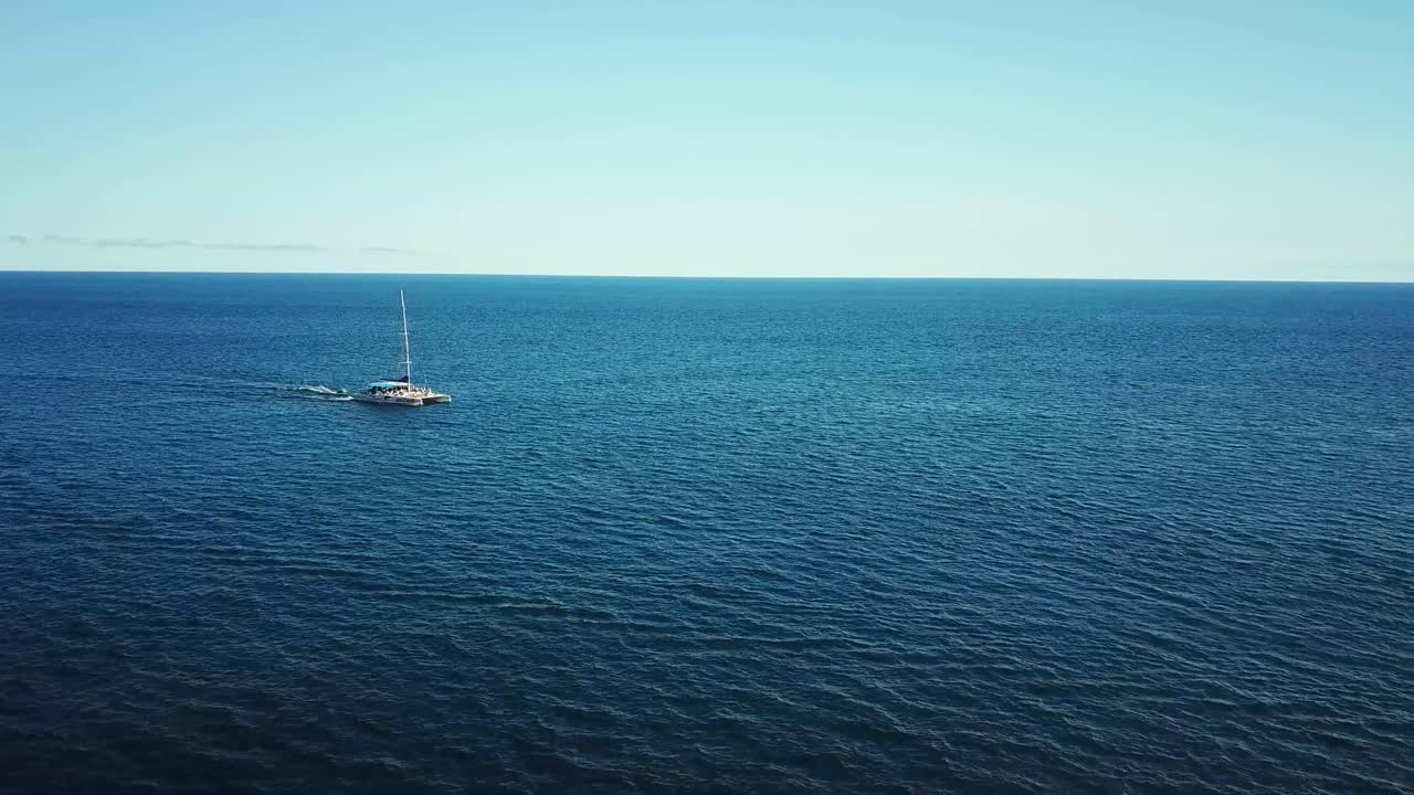 A sailboat cruises through the tranquil blue waters of the open sea, near Funchal Madeira, under a clear sky. The vast expanse of the ocean meets the horizon, creating a serene and picturesque scene