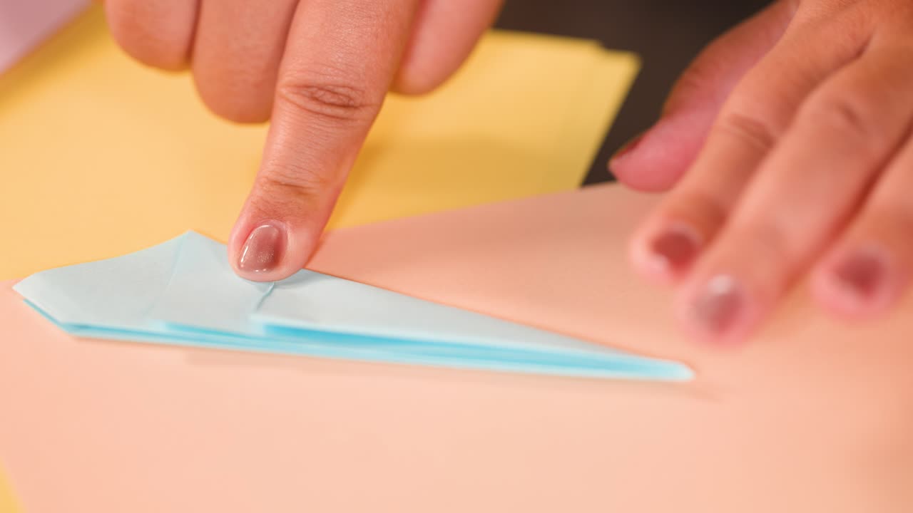 Nærbillede af hænder, der omhyggeligt folder blåt papir til en origami-form på et skrivebord