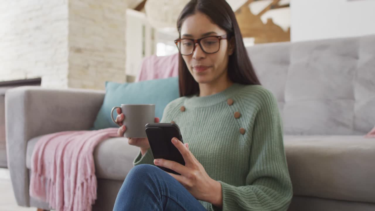 mujer biracial usando un teléfono inteligente y sonriendo en la sala de estar