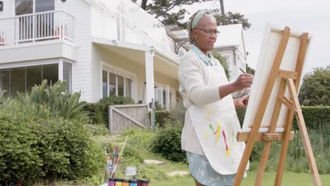 Mujer-Afroamericana-Mayor-Pintando-Sobre-Caballete-De-Madera-En-El-Jardín,-Cámara-Lenta