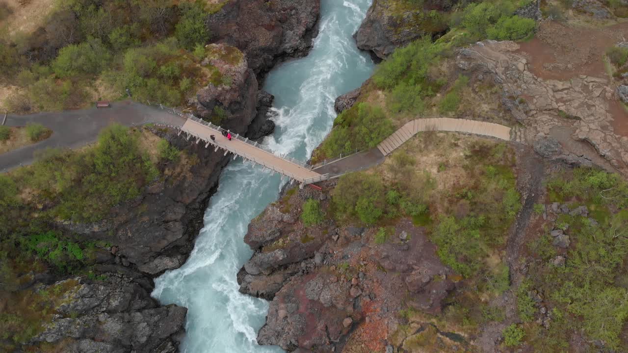 Aerial view going over the waterfalls Barnafossar and Hraunfossar with some tourists standing on the plateau and looking out over the beautiful Icelandic landscape with lush green trees and rocks