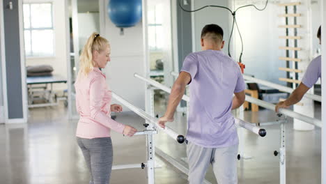 man in rehabilitation using parallel bars with therapist in physical therapy center