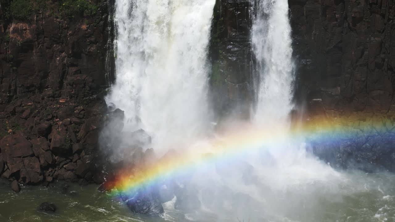 hermosos arco iris brillantes cubiertos por enormes cascadas en las cataratas de iguazu, grandes cuerpos de agua que caen del borde de un acantilado rocoso oscuro sobre un colorido arco iris en las cataratas de iguazu, brasil