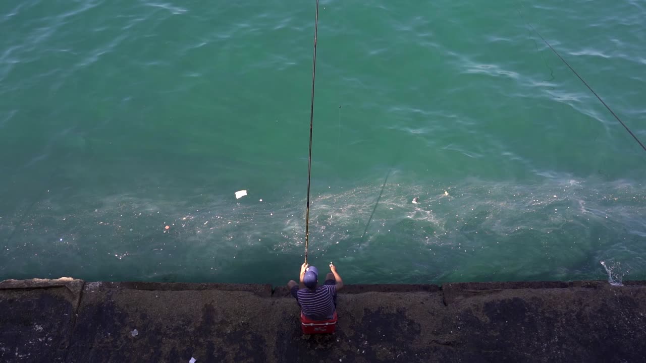 pescador anónimo sentado en un terraplén a la orilla del mar con una caña