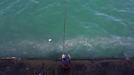 pescador anónimo sentado en un terraplén a la orilla del mar con una caña