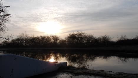 Sunrise-glowing-over-waterfront-narrow-canal-channel-rippled-frosty-water-early-morning