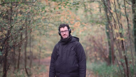 cheerful young german gentleman with glasses and beard, stands amidst the hues of an autumnal european mixed forest, grinning warmly and offering a friendly greeting