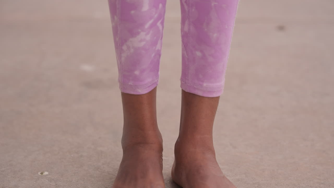 Ett barns fötter på dammig trottoar, lila leggings synliga, tårna spretar mot varm betong, närbild på hudens textur och sandkorn, lugn paus som framkallar oskuld och tyst vardag.