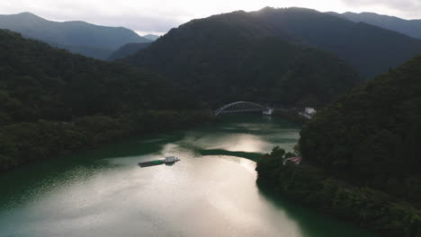 Die-Helle-Sonne-Reflektiert-Das-Ruhige-Wasser-Des-Okutama-sees-Mit-Mito-brücke-Und-Grünen-Bergen-Im-Hintergrund