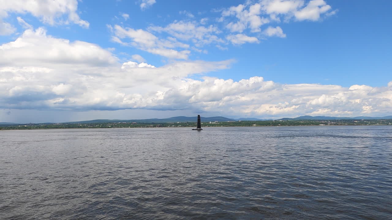 широкий вид парусной лодки, плавающей на спокойной воде вдоль побережья с облачным небом на горизонте, регион квебек, канада