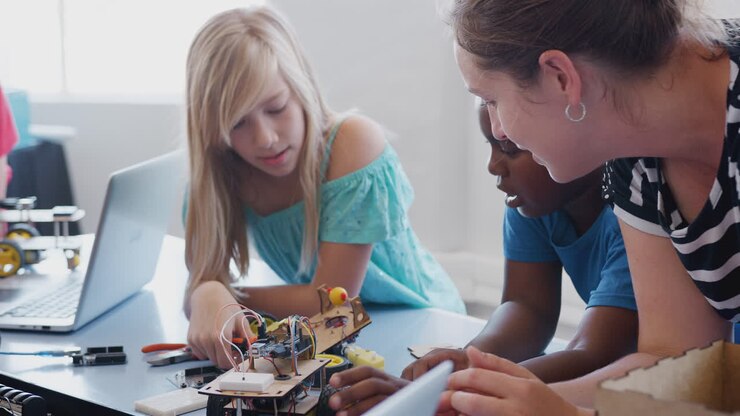 Students With Female Teacher In After School Computer Coding Class Learning To Program Robot Vehicle