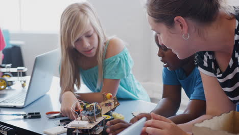 students with female teacher in after school computer coding class learning to program robot vehicle