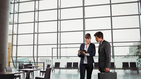 caucasian male and female in suit in an office shaking hands ans watching a tablet